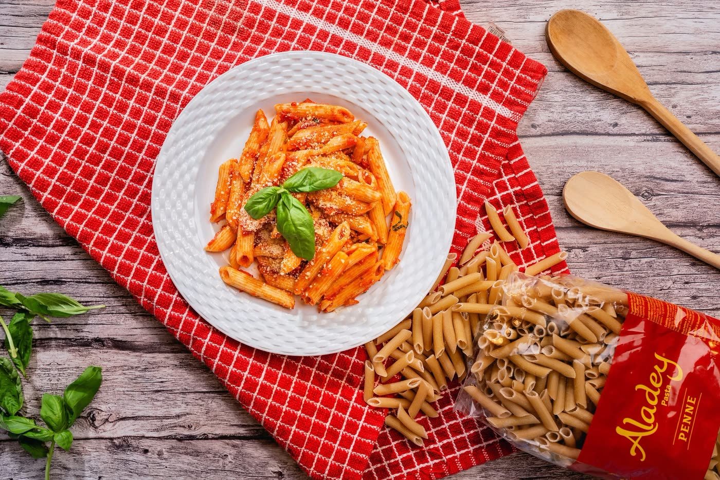 A plate of Aladey Penne in tomato sauce with basil, beside the 500 g pack